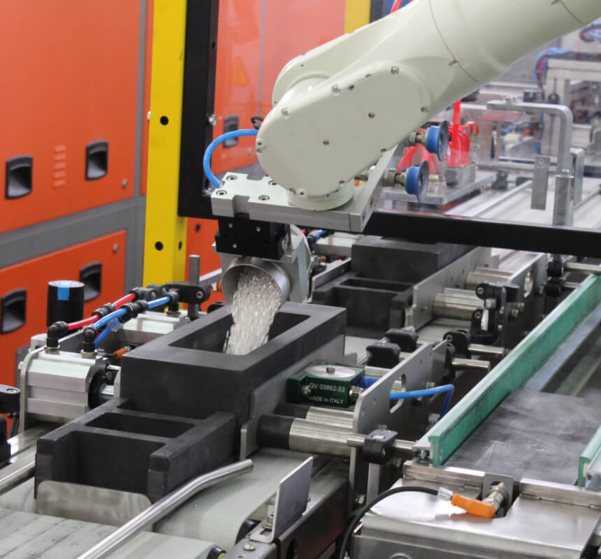 Un braccio robotico versa materiale granulato in uno stampo nero rettangolare su una linea di produzione in una fabbrica.