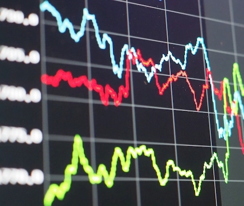 A close-up of a digital screen displaying multiple fluctuating line graphs in blue, red, and green, representing financial or stock market data against a black background with a grid and numbers on the side.