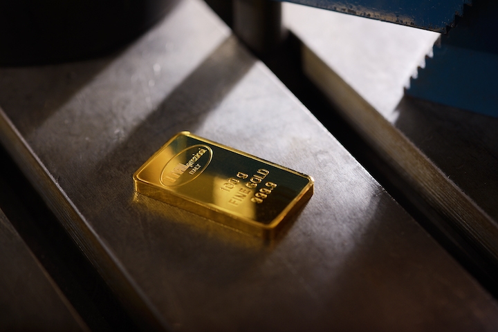 A single gold bar with inscriptions rests on a metal surface, illuminated by light from above.