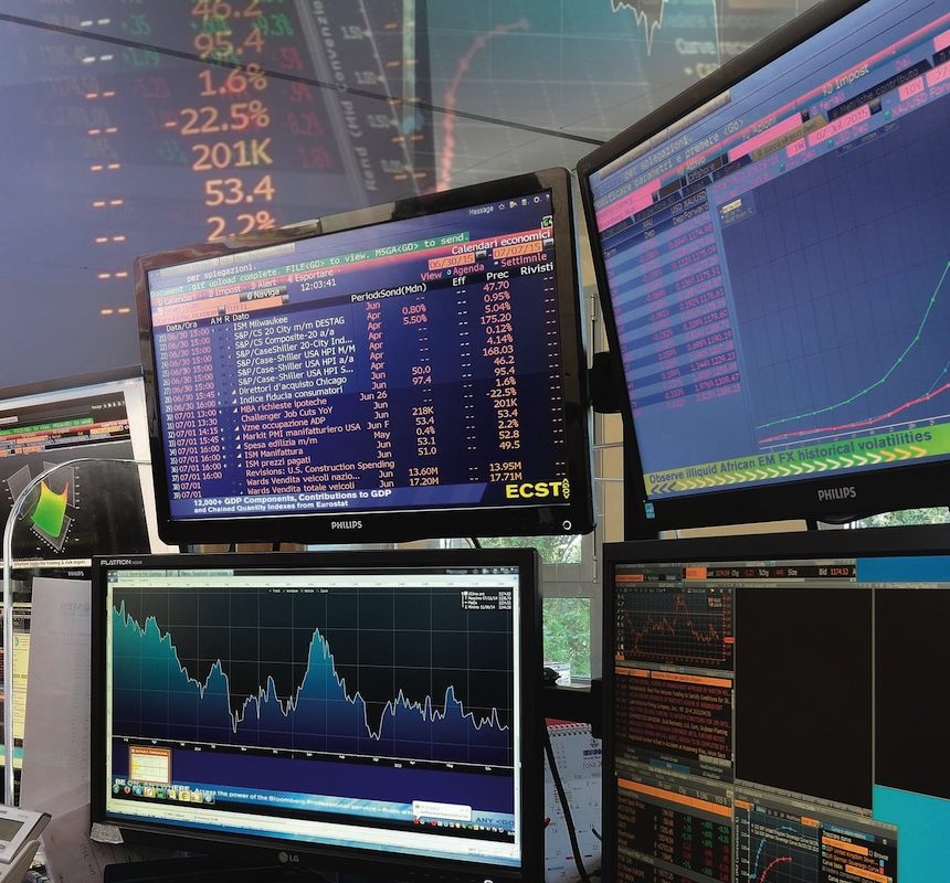 Trading online Più monitor di computer visualizzano dati finanziari, grafici azionari e di mercato in un ambiente di trading office.